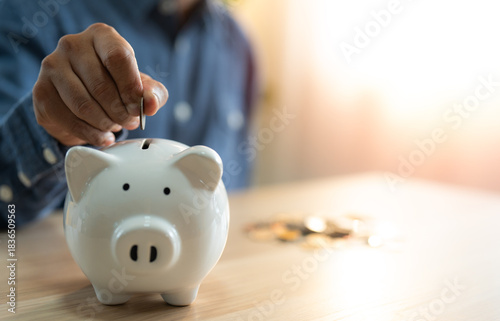 A man hand putting coins into a white piggy bank for account save money. Planning step up, saving money for future plan, retirement fund. A business investment-finance accounting concept.