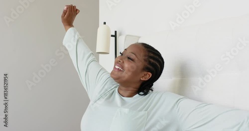 Mid adult African American woman waking up in bed, stretching arms over headboard feeling refreshed
