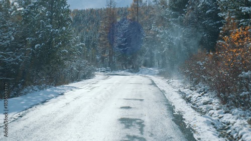 First-person view of a car driving on a dangerous, icy road through a snowy mountain forest during a winter journey, showcasing the slippery conditions and the beautiful, frozen landscape