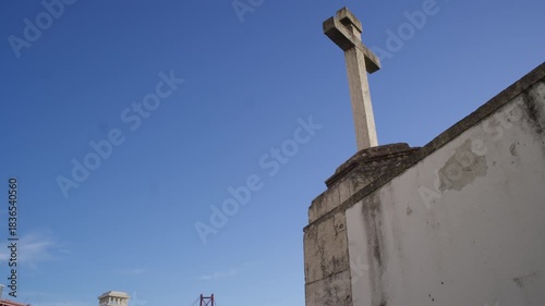 Stone cross at Santo Amaro chapel viewpoint overlooking the 25 de Abril bridge under clear blue sky in Lisbon, Portugal
