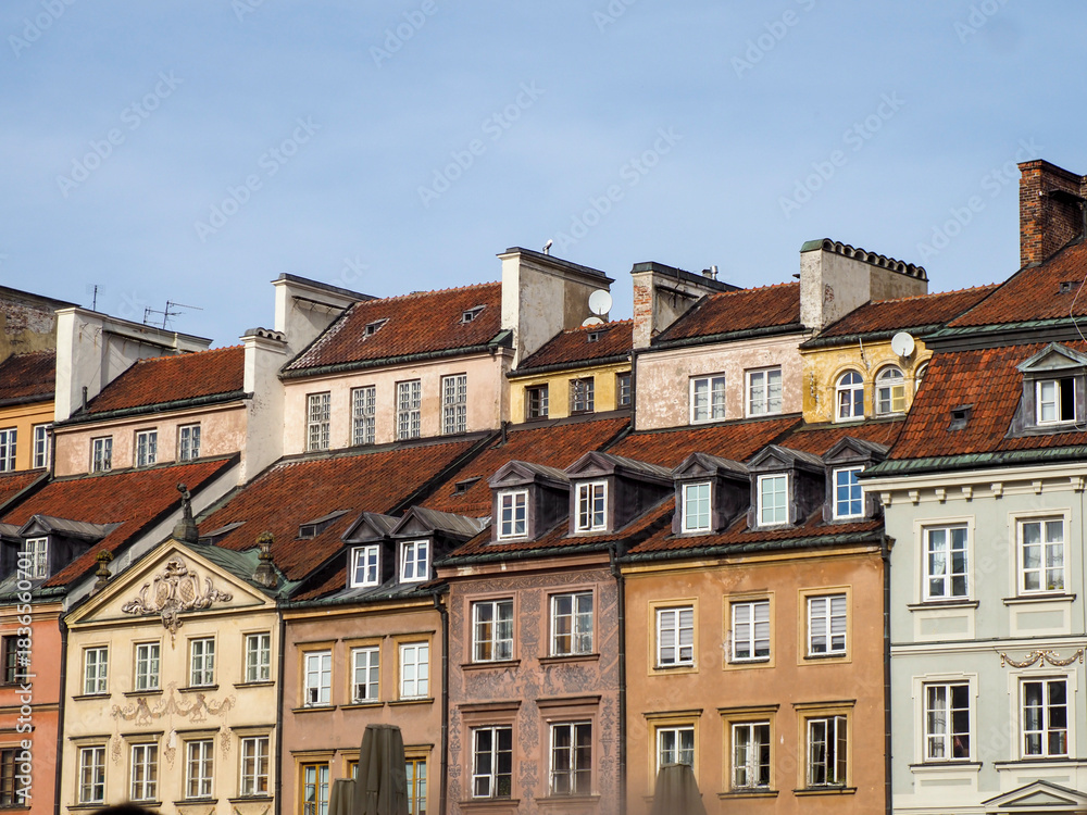 Fototapeta premium General view of the unified facades of historic townhouses with varying pastel colors and red tiled roofs in Warsaw Old Town, Poland.
