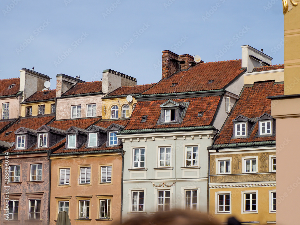 Fototapeta premium Wide shot of multiple rows of beautifully restored colorful townhouses with red roofs in Warsaw Old Town on a clear day.