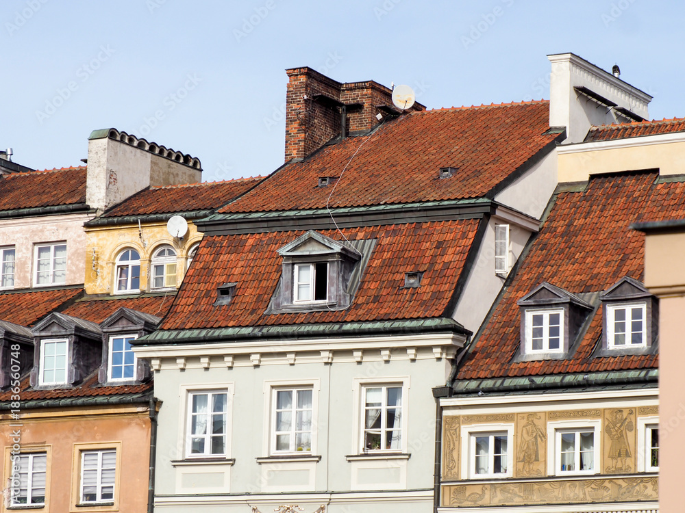 Fototapeta premium Picturesque panorama of colorful facades and steep red tiled roofs of historic townhouses in Warsaw Old Town against a blue sky.
