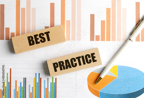 Text best practice written on wooden blocks with financial graphs and pen in background