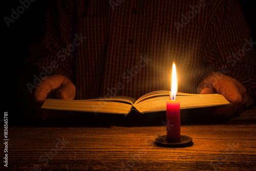Hands hold an open book in the warm glow of a candle. This calm scene reflects the magic of reading by candlelight and offers a moment of peace in a hectic world.