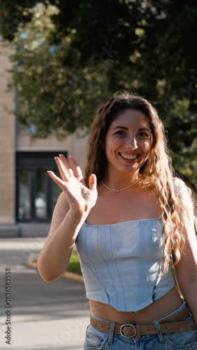 A portrait of a cheerful girl with long curly hair smiling at the camera. A close-up portrait of a friendly young woman in casual clothes against a blurred city background. Outdoors.