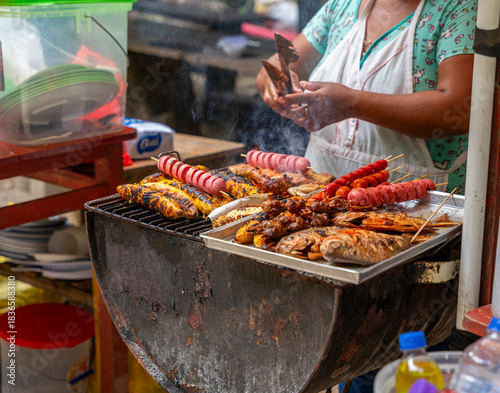 Tableau sur toile Peruvian Amazon street vendor grilling fish, chicken, plantains, and skewers over open flame in rustic outdoor food scene