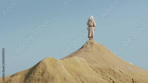 A robed Wanderer stands facing the horizon on a desert peak. Christian and spiritual concept