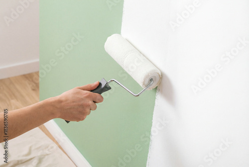 Hand using a paint roller to cover a mint green wall with white paint. Theme of renovation, home improvement and interior transformation.