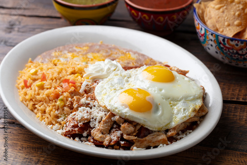 Overhead angle of Mexican fried eggs sunny-side up with rice, beans, cheese, sour cream, and Ranchero sauce on a white plate. 