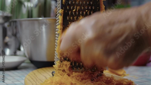 Close-up, elderly woman's hand grating a pumpkin on a kitchen grater to make a pie