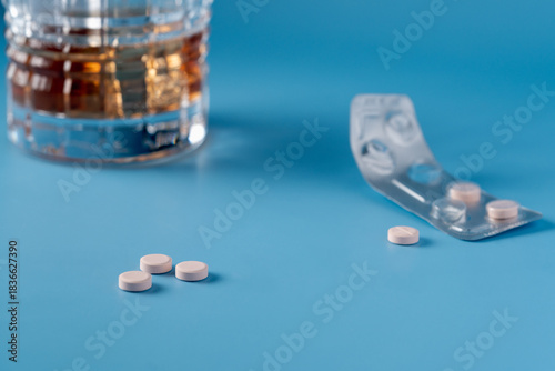 A blurred glass of alcohol in the background and a pack of pills. Three pink tablets are sitting on the table ready to use. Focus on foreground