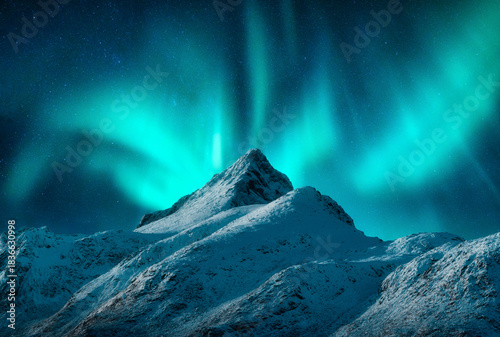 Northern lights over the snowy mountains at night in Lofoten, Norway. Aurora borealis above the snow covered rocks. Winter landscape with polar lights, mountain peak. Starry sky with green aurora