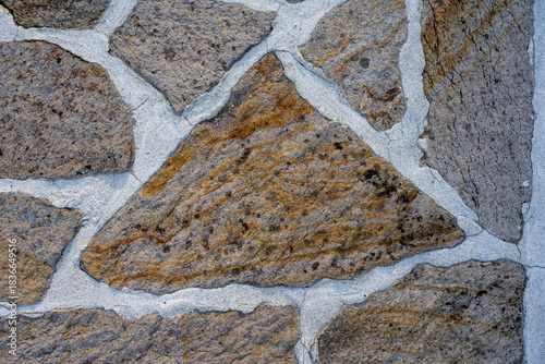 Close-up view of an irregular masonry wall composed of textured natural stones and light mortar joints. 