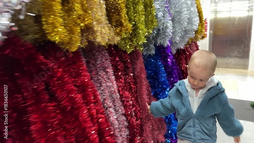 Little child touching multicoloured tinsel. Christmas holidays content. 4K