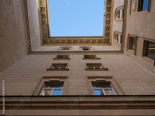 Low angle architectural shot looking up at the courtyard facade of a large, imposing
stone building with neo-classical or Socialist Classicism elements. The image focuses on
the uniform beige stonewor