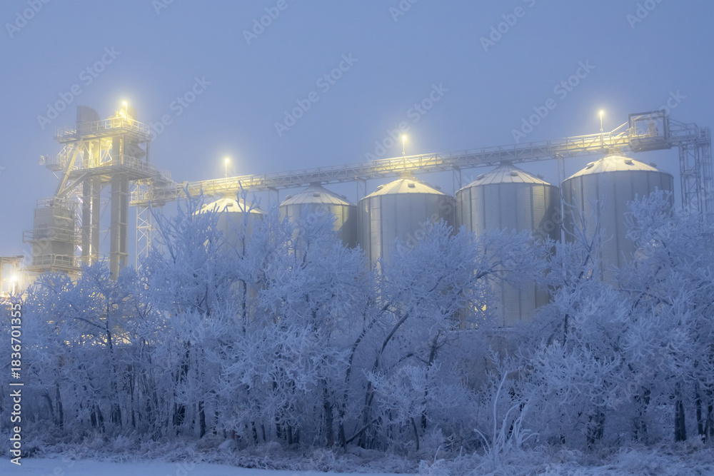 Naklejka premium Lights on grain elevator storage in foggy winter night.