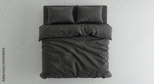 A neatly made bed with dark grey duvet and two matching pillows rests on a light background, viewed from directly above, offering clean copy space.