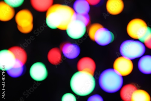 Blurred view of bright Christmas lights on dark background, bokeh effect