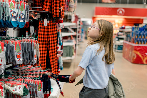 A girl chooses socks or pajamas with a Christmas print. Holiday shopping concept. Christmas gifts.