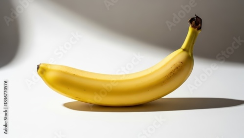 A single ripe yellow banana resting horizontally on a clean white surface with subtle shadows.