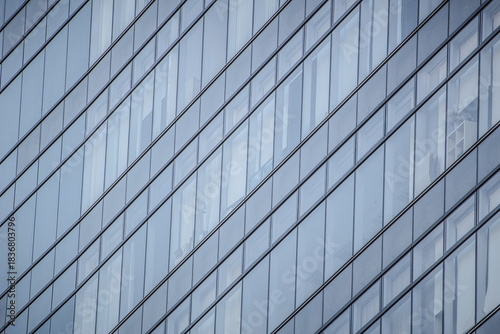 A modern glass building with diagonal panel arrangement, reflecting surroundings and revealing interior elements.