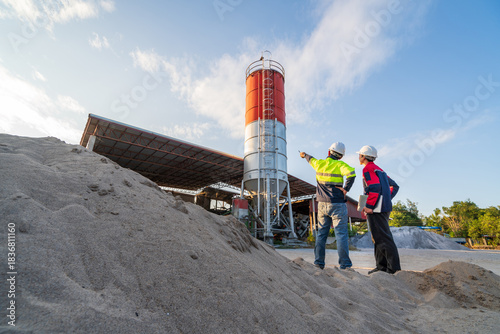 Photos Two engineers inspect aggregate piles and a concrete batching plant at sunset, focusing on material management and small business operations