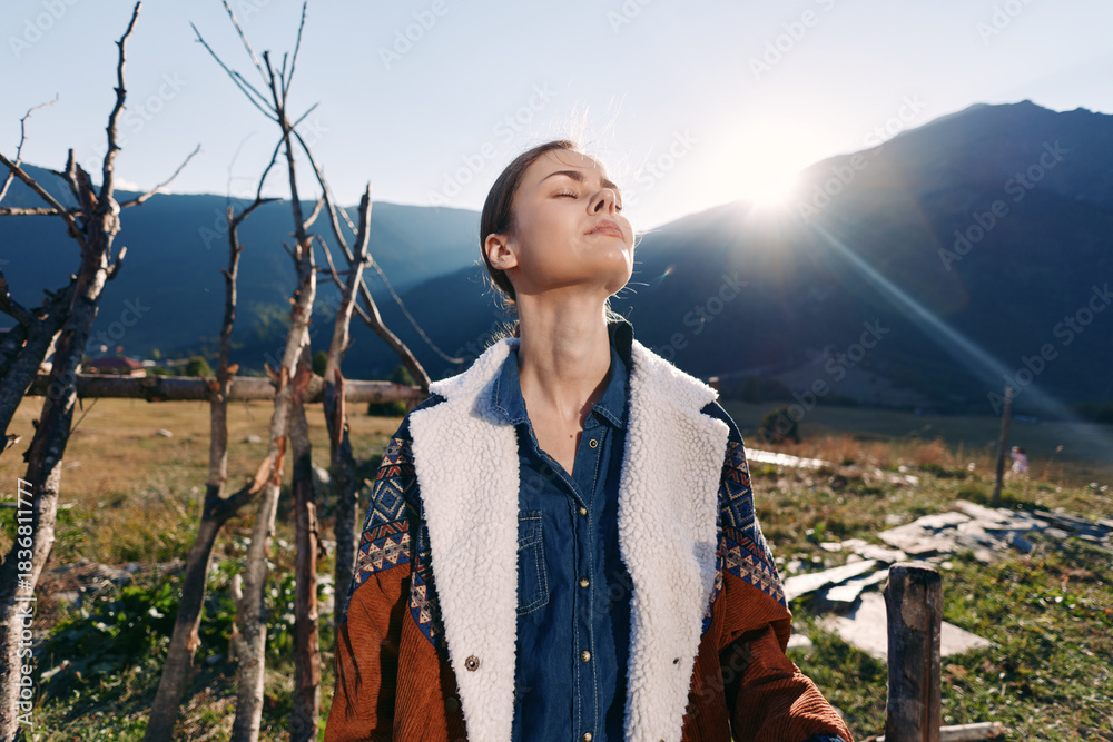 Naklejka premium woman outdoors mountains sunlight nature portrait rural jacket traveler relaxation, portrait of a relaxed young woman in a denim shirt and warm jacket breathing fresh mountain air