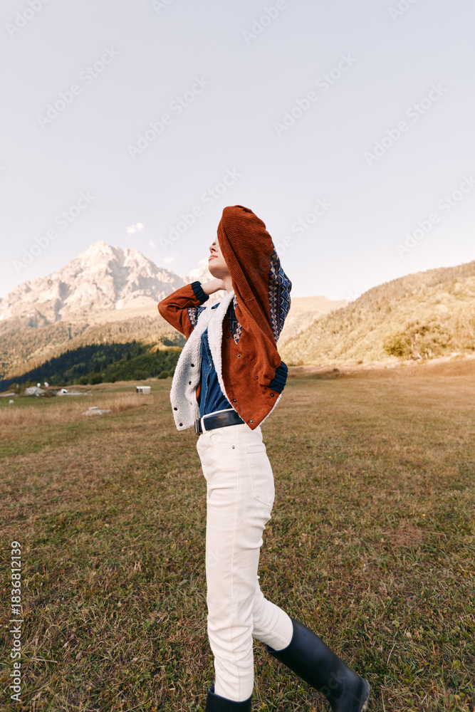 Obraz premium Woman in mountain meadow wearing autumn fashion jacket and boots, portrait of relaxed style outdoors. White pants, knit sweater and scenic landscape for travel and lifestyle.