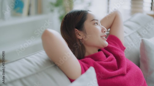 Relaxed young Asian woman enjoying rest on comfortable sofa, calm attractive girl relaxing on couch, breathing fresh air with eyes closed, meditating at home