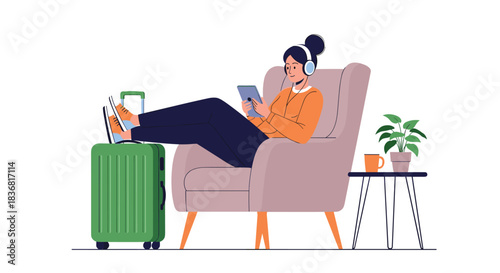 Young woman relaxing in an armchair with her feet on a suitcase, listening to music and using a tablet while waiting to travel.