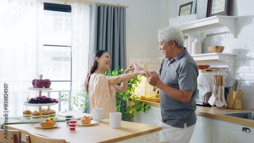 Happy cheerful senior Asian couple family parents dancing together in the kitchen, preparing cooking food meal for romantic dinner, spending time together
