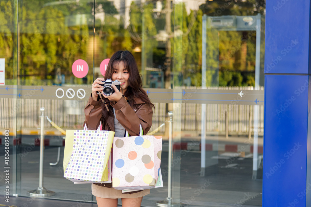 Fototapeta premium Asian woman shopping for fashion, bags, enjoying lifestyle, people shop at city mall, preparing for black friday, capturing moments with retro camera