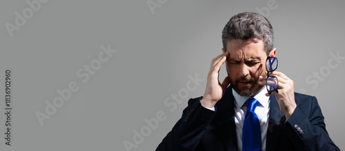 Stressed business man having headache. Tired businessman in suit is working overtime and has headache. Overworked man suffers from headache, banner with copy space. Migraine at work.