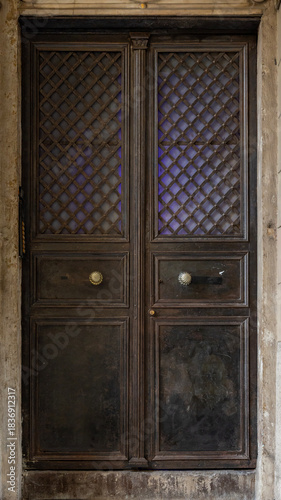 Classic wooden double door with decorative panels and vintage handles, framed by marble walls, showcasing traditional architecture and elegant historic craftsmanship.