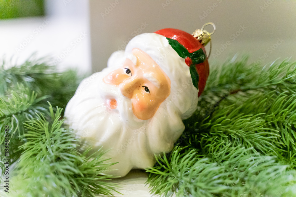 Obraz premium A charming Christmas setup featuring a Santa Claus figurine surrounded by small festive decorations and wrapped presents. The scene highlights warm holiday cheer with miniature ornaments, gift boxes, 