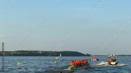 Warsaw, Poland - August 28, 2025: Group of people in orange life jackets paddling on a dragon boat, camera follows action across the water, showcasing vibrant summer activity