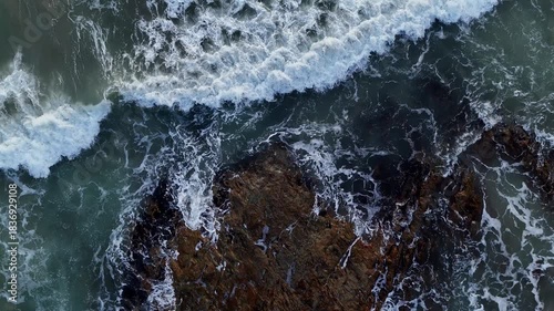 Giant ocean waves crashing and foaming on empty sand tropical beach with big rock stones