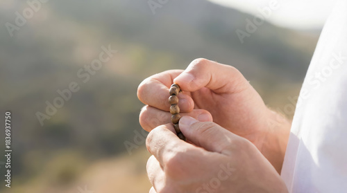 Close-up of male hands counting brown wooden rosary beads during prayer outdoors