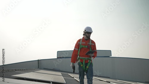 Blue collar worker is inspecting solar panel at rooftop of factory. Energy, sustainability.
