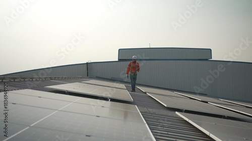 Blue collar worker is inspecting solar panel at rooftop of factory. Energy, sustainability.