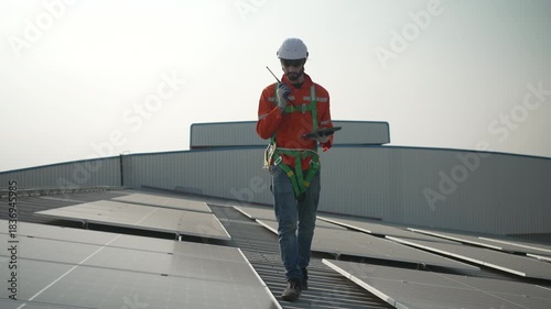 Blue collar worker is inspecting solar panel at rooftop of factory. Energy, sustainability.