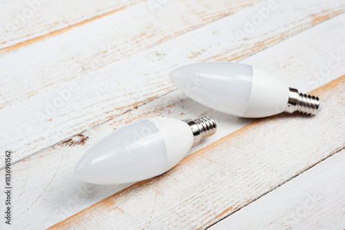 Two LED lamps with E14 sockets lying on a wooden surface.