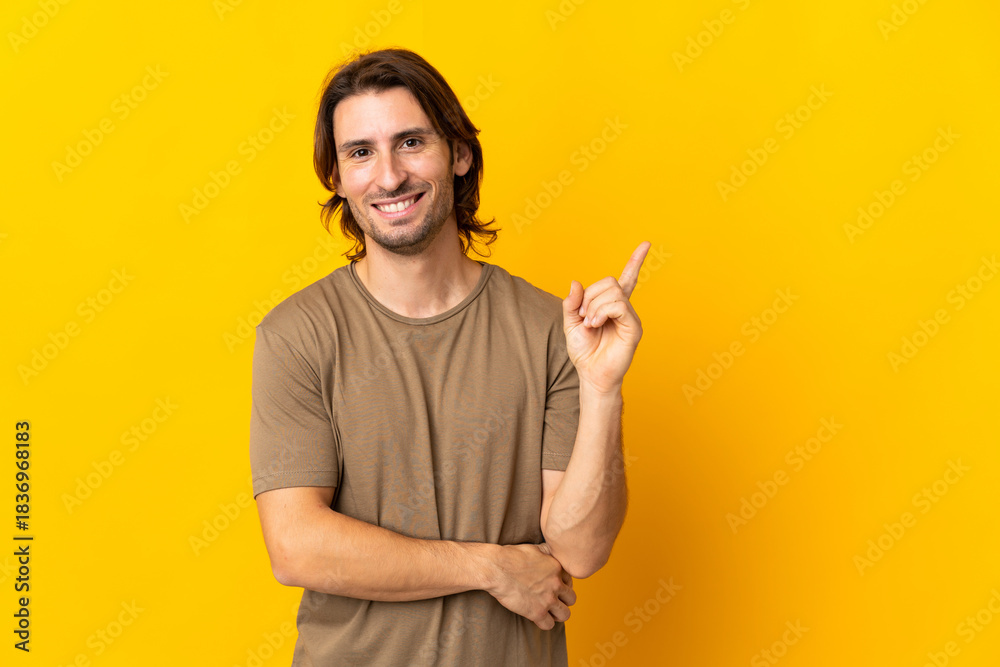 Fototapeta premium Young handsome man isolated on yellow background happy and pointing up