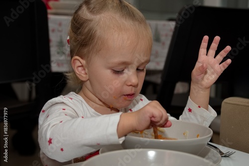 Little girl sitting at the table and eating soup