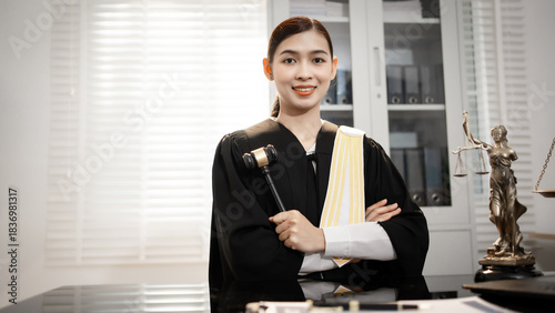 Photography A confident Asian female lawyer in a professional robe sits at a desk with a laptop and Lady Justice statue, specializing in modern international trade, cyber security, and data protection laws