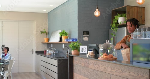 African-American barista bagging croissants while customer entering cafe to place order, copy space