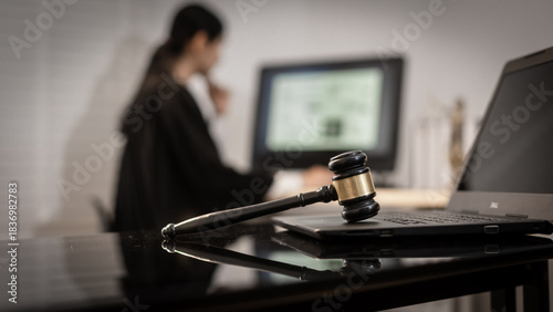Photography A focused Asian female judge works on complex cases involving cyber law, data protection, and digital rights, with the gavel and laptop symbolizing modern legal authority