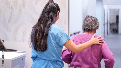 Granddaughter assisting elderly grandmother walking in nursing home