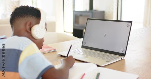 At lesson start lifting pencil, student writing notes, glancing at laptop to follow online lesson